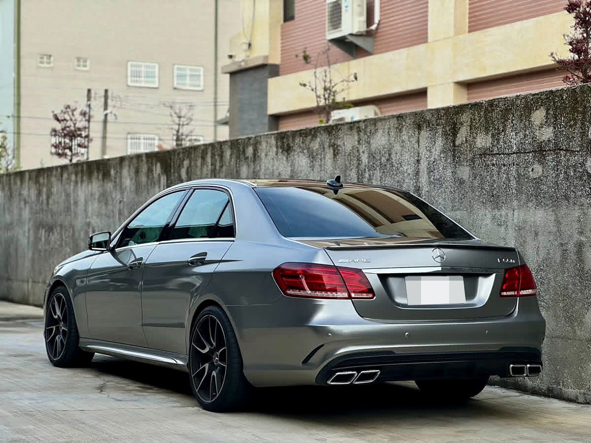 Silver Mercedes-Benz E-Class sedan with quad exhaust outlets and black wheels, rear three-quarter view.