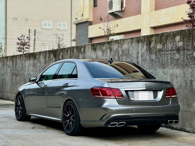Silver Mercedes-Benz E-Class sedan with quad exhaust outlets and black wheels, rear three-quarter view.